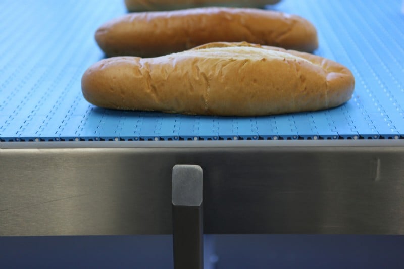 Bread conveyed on a stainless steel blue belt conveyor.