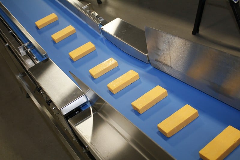 Stainless steel conveyor with blue belt carrying cheese